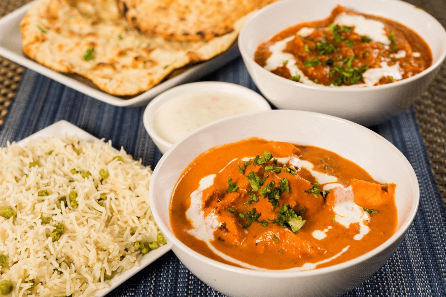 dishes of butter chicken and other authentic Indian food served with naan and rice